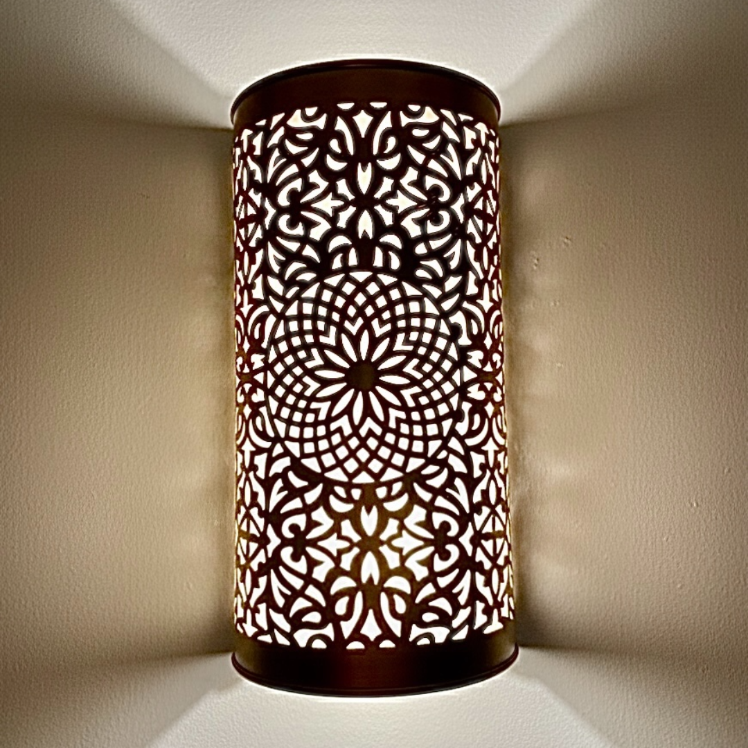 A close-up view of a handcrafted brass wall sconce with intricate Moroccan geometric patterns glowing on a wall.