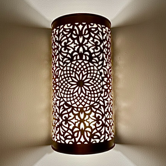 A close-up view of a handcrafted brass wall sconce with intricate Moroccan geometric patterns glowing on a wall.
