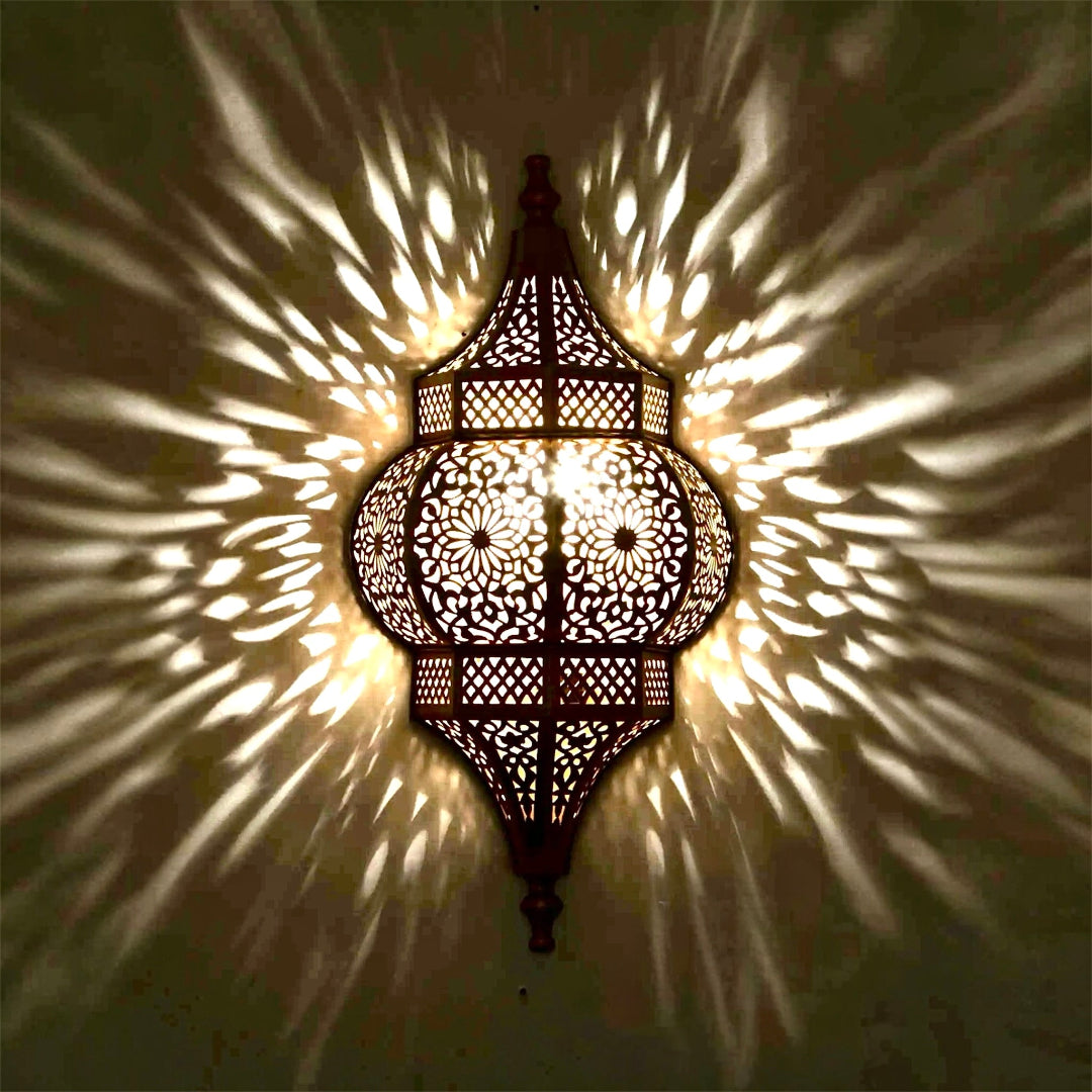 Handmade brass wall sconce featuring intricate Moroccan filigree patterns, casting decorative shadows on a wall in a modern luxury interior.