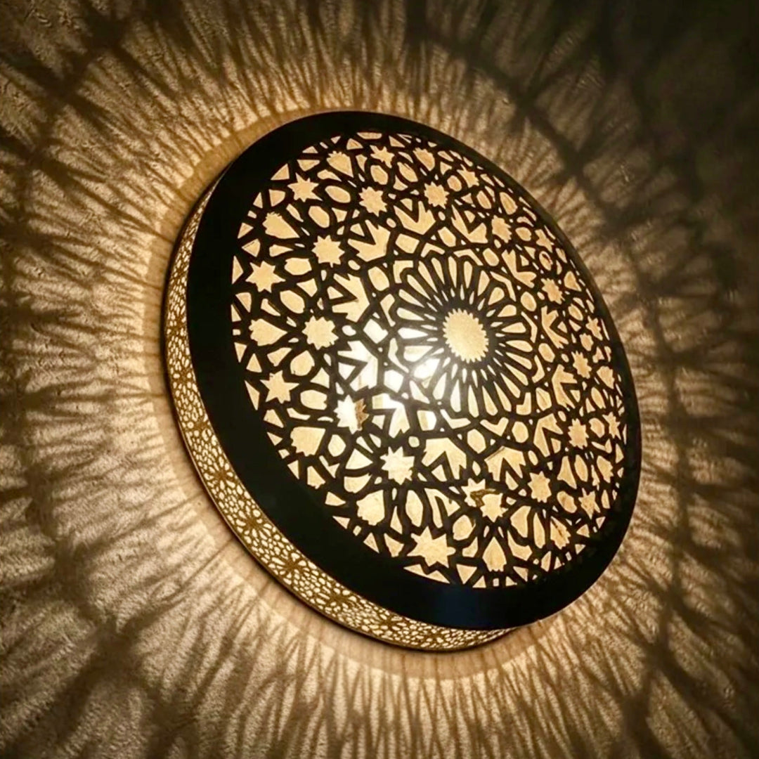 An illuminated handmade brass wall sconce lamp featuring traditional Moroccan geometric cutouts casting warm ambient light patterns.⁠