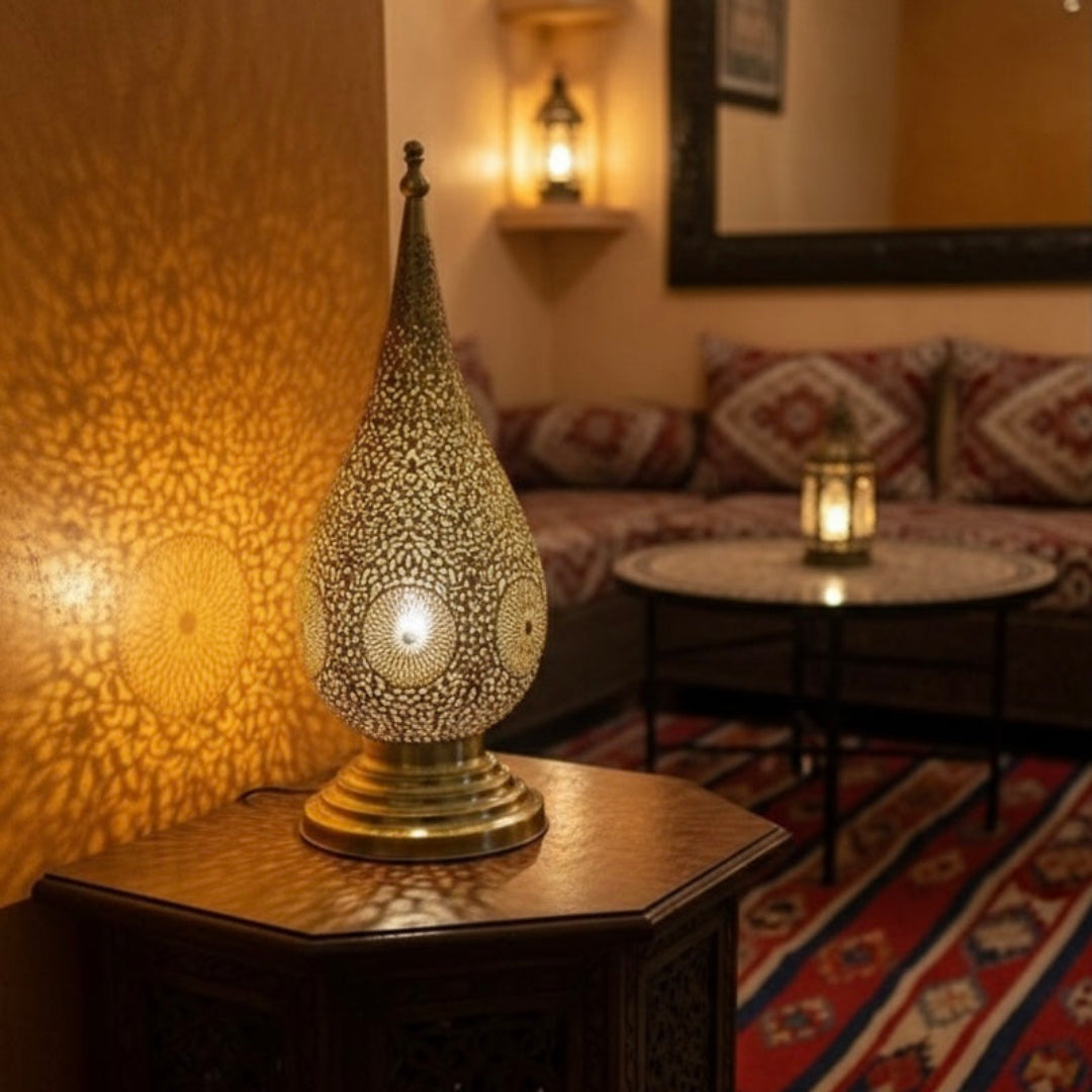 Handmade Moroccan brass lamp with intricate filigree casting floral shadow patterns on a warm wall.
