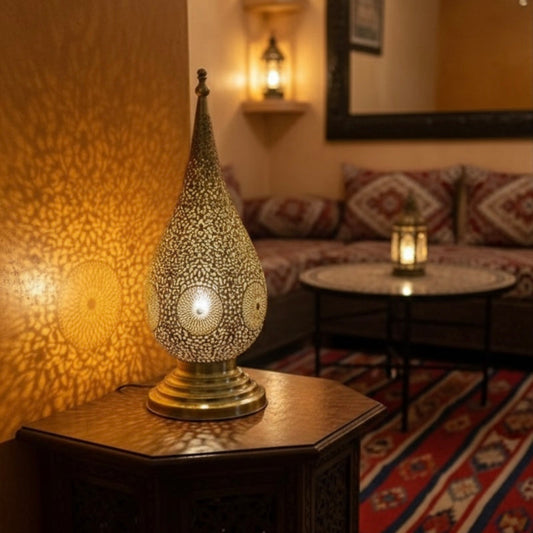 Handmade Moroccan brass lamp with intricate filigree casting floral shadow patterns on a warm wall.
