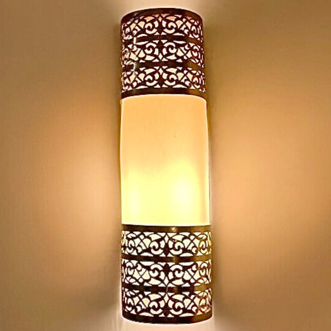  Front view of a cylindrical handmade Moroccan brass wall lamp featuring traditional geometric fretwork and a warm glowing center.