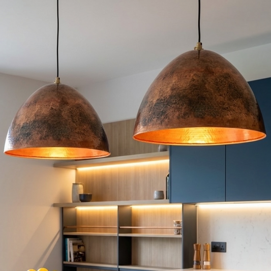 Two custom handmade Moroccan dome lights in aged copper hanging above a marble kitchen counter next to navy blue cabinets