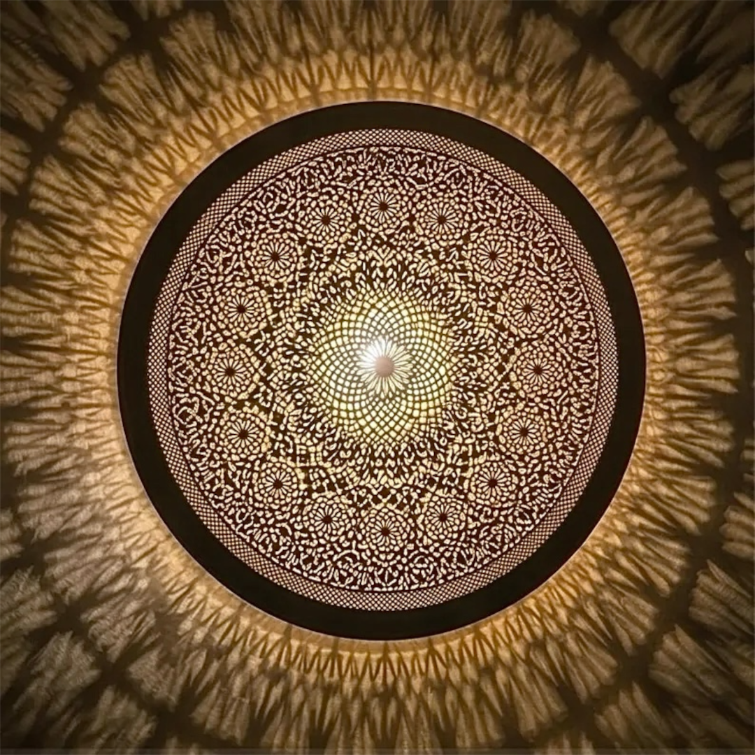 Close-up details of a handmade Moroccan flush mount brass lamp showing intricate geometric filigree patterns and warm shadows.