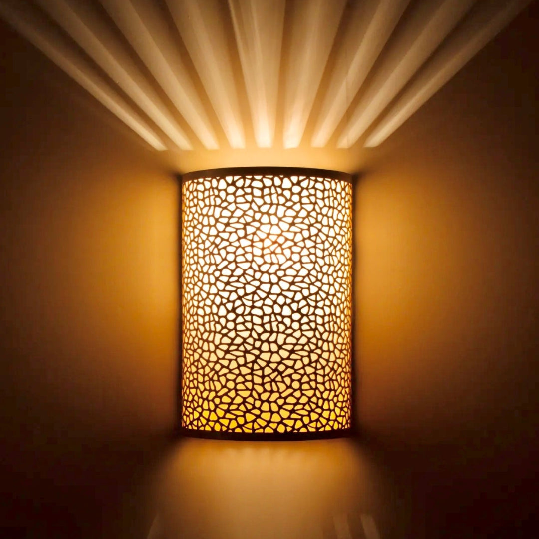 Close-up of a handmade Moroccan wall sconce featuring intricate organic perforations in polished brass, artisanal lighting detail.