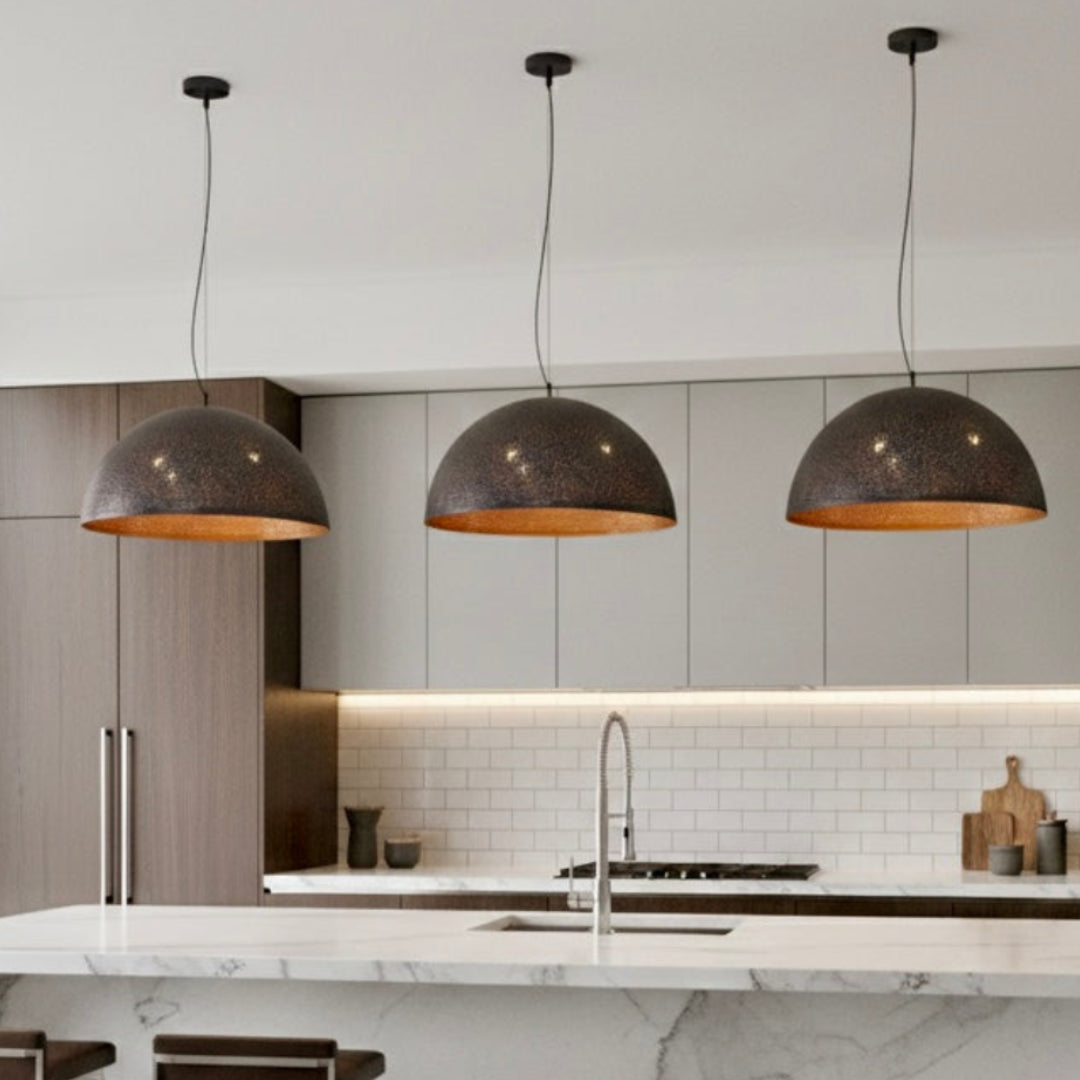 Three contemporary hammered brass pendant lamps installed over a white marble kitchen island in a minimalist interior.
