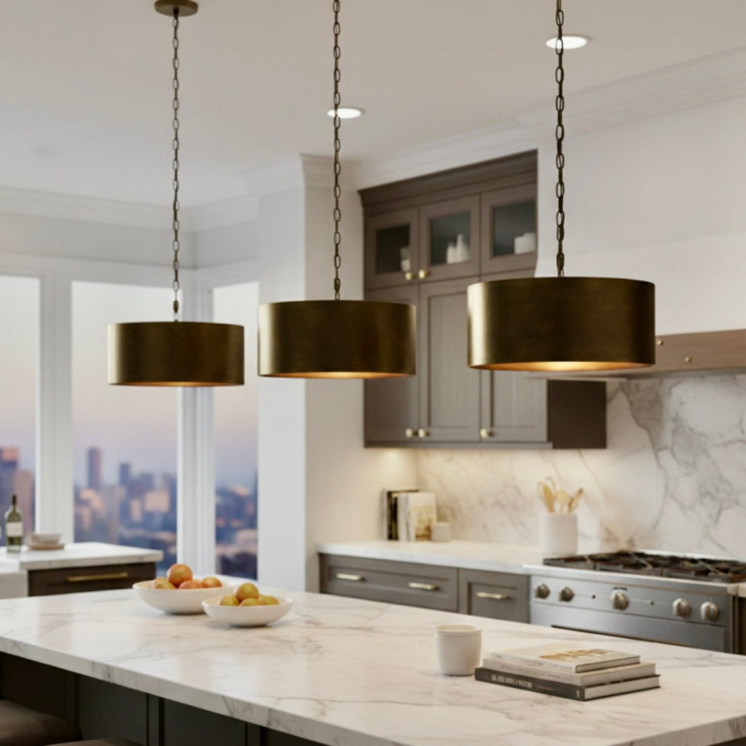Trio of handmade hammered brass drum lights installed over a white marble kitchen island with dark cabinetry