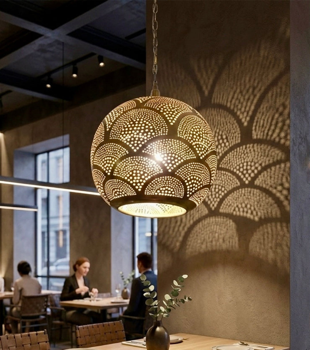  Professional restaurant interior featuring a Moroccan brass pendant light as a centerpiece, casting beautiful shadows on a textured pillar near dining tables.