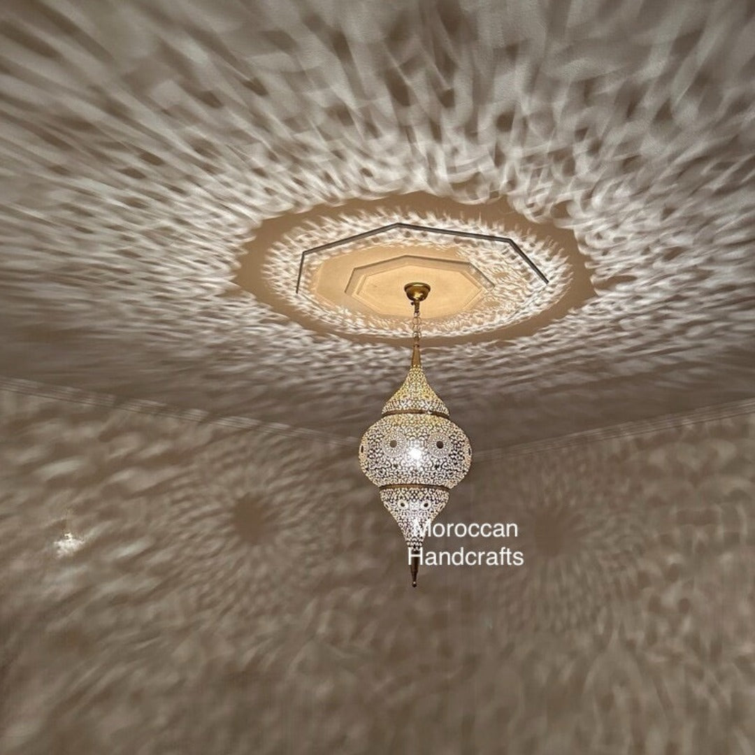 A handcrafted Moroccan brass pendant lamp casting intricate geometric shadows on the ceiling of a modern bar and restaurant.