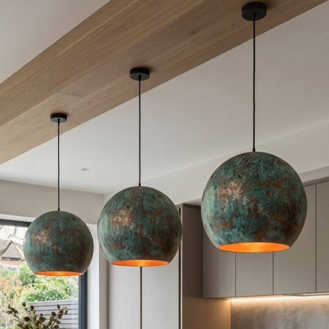Trio of modern Moroccan brass and green copper pendant dome lights suspended over a minimalist black marble kitchen island