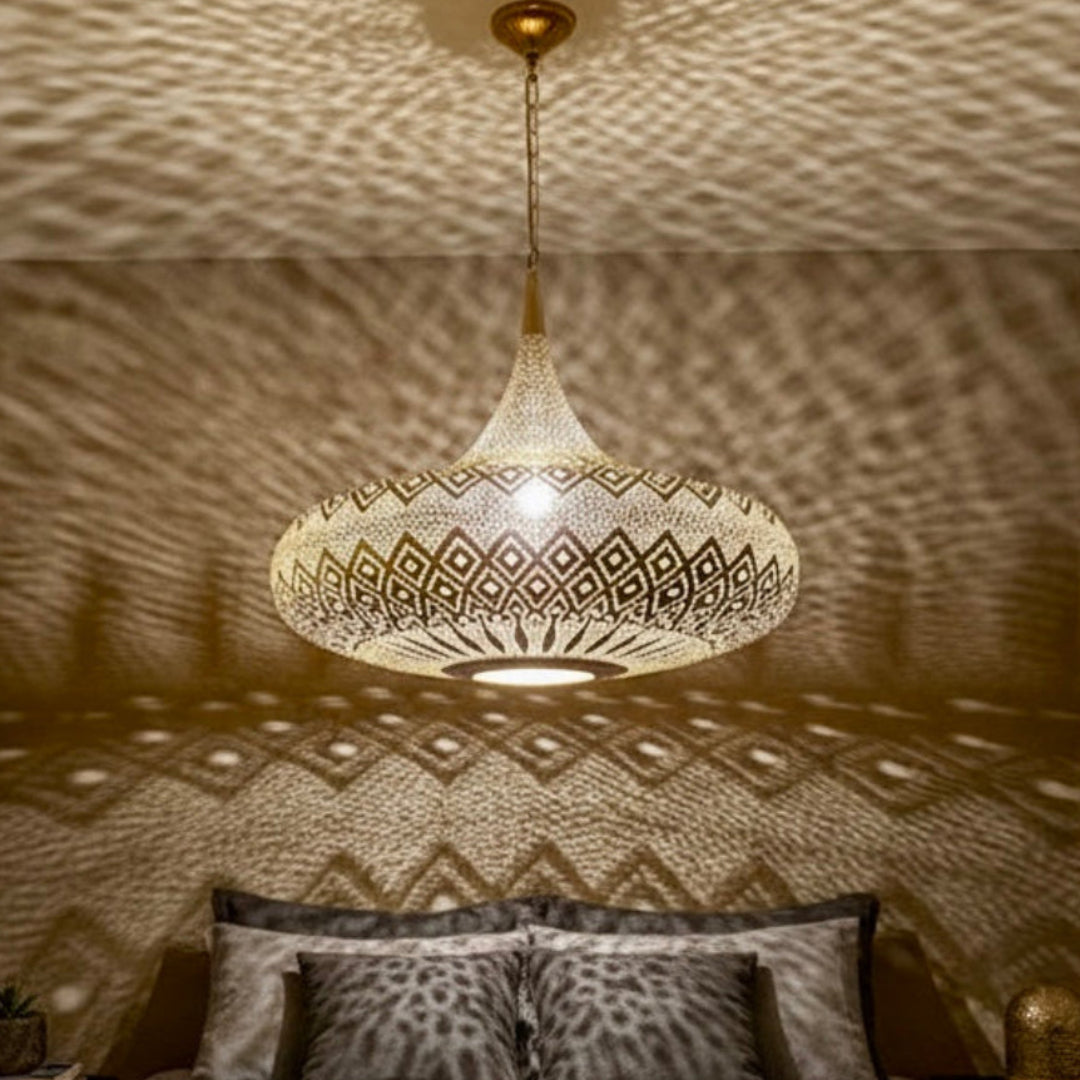 A large handmade Moroccan brass lamp hanging in a modern living room, casting intricate geometric shadow patterns on white walls.