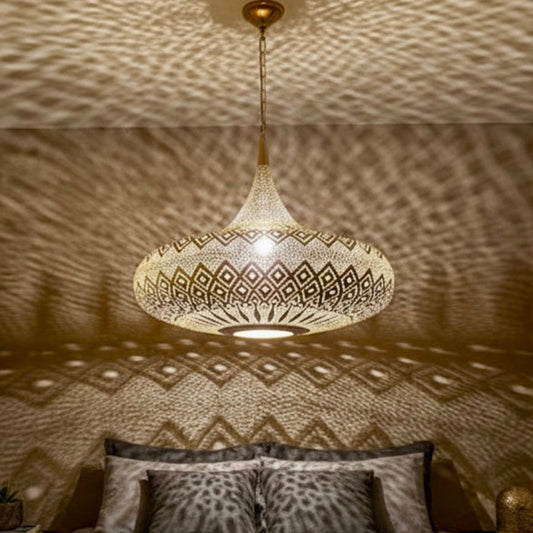A large handmade Moroccan brass lamp hanging in a modern living room, casting intricate geometric shadow patterns on white walls.