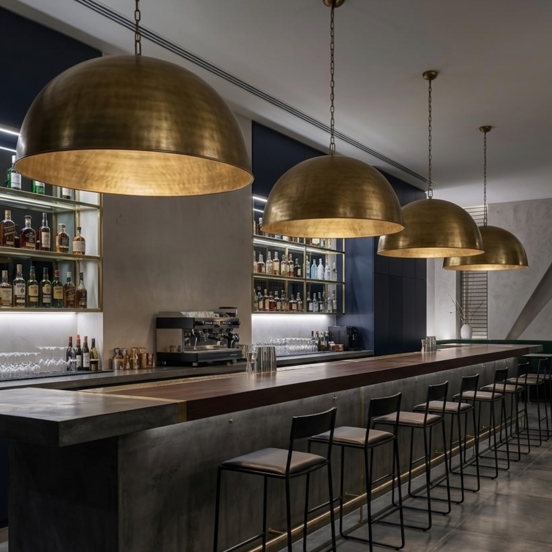 Row of four hammered brass dome pendant lights illuminating a sleek modern commercial bar with dark interior design