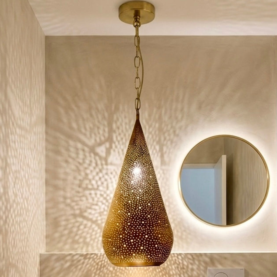 Teardrop brass Moroccan lamp reflecting intricate light patterns on a minimalist bathroom wall with a round backlit mirror.