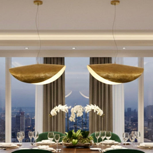 Three large handmade Moroccan brass pendant lamps with a wavy crescent design hanging over a long wooden dining table in a modern industrial interior.