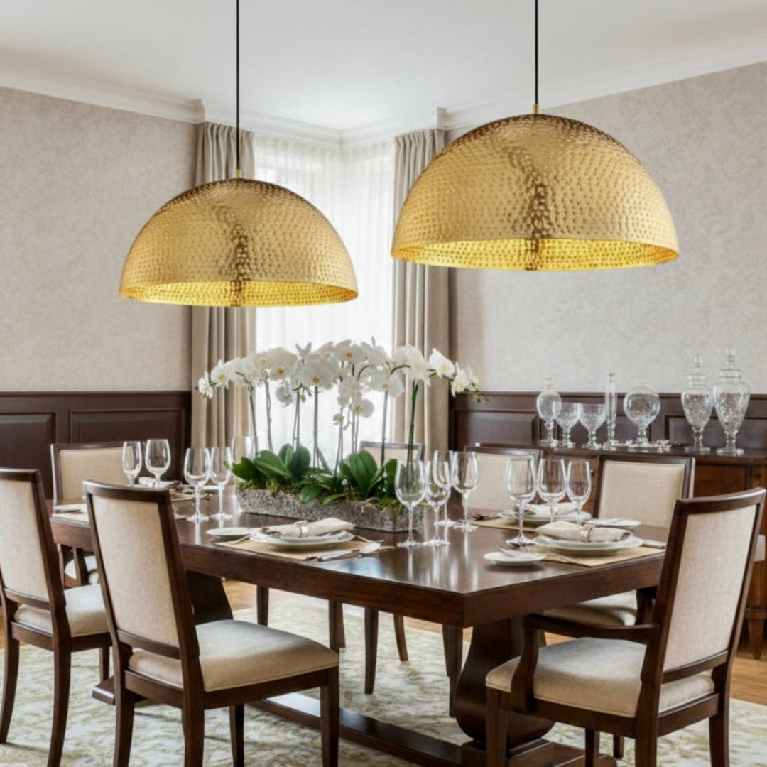 Pair of large modern Moroccan brass dome lamps hanging over a formal wooden dining table with elegant table setting.