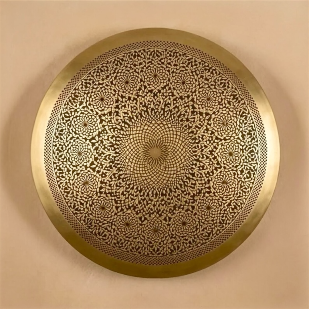 Modern Moroccan round brass wall sconce installed on a concrete texture wall projecting a large sunburst shadow pattern in a minimalist interior.