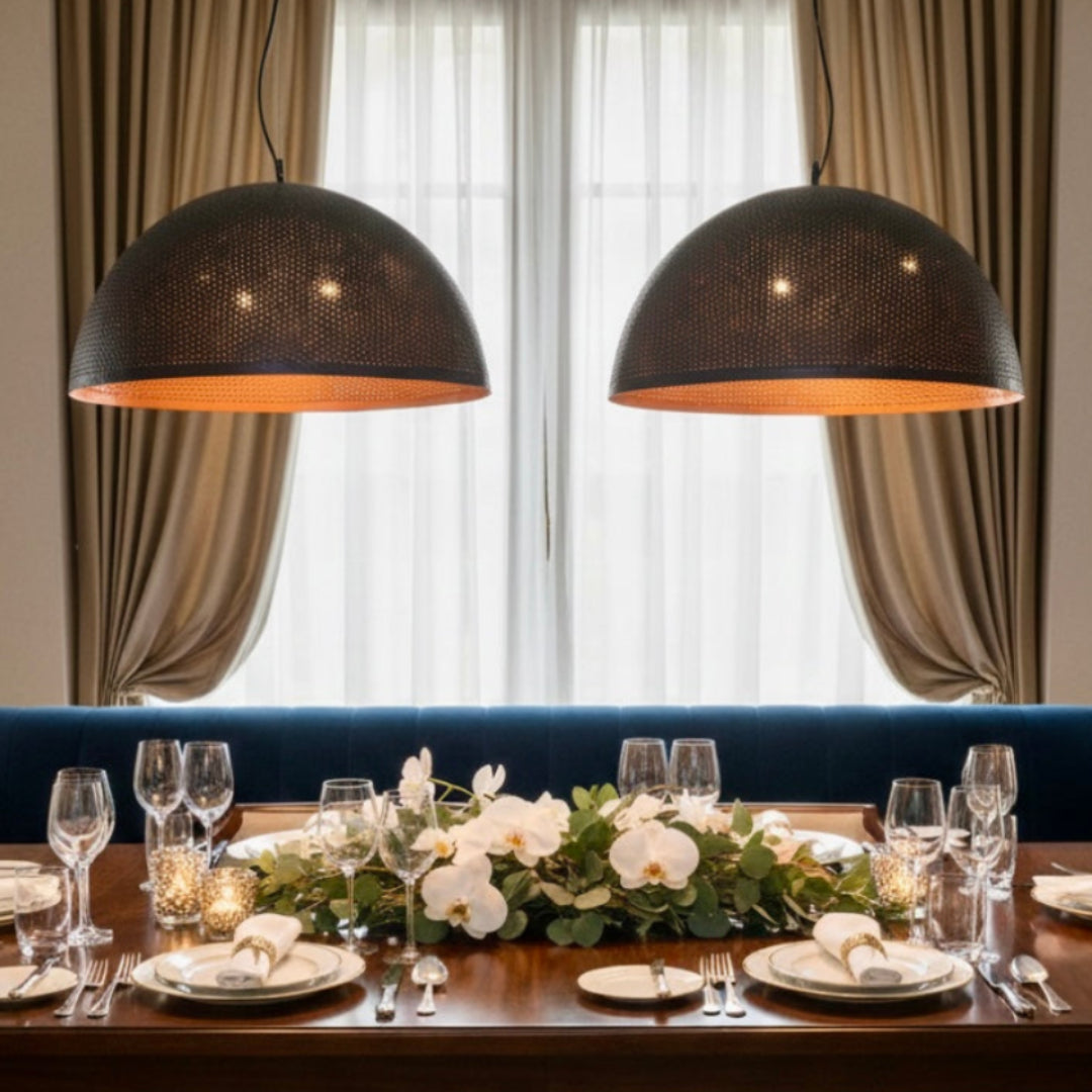 Two large handmade hammered brass dome pendant lights hanging above a modern dining table with a city view.