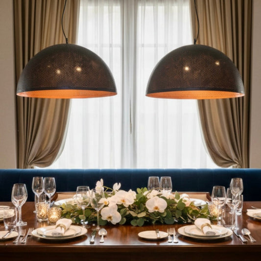 Two large handmade hammered brass dome pendant lights hanging above a modern dining table with a city view.