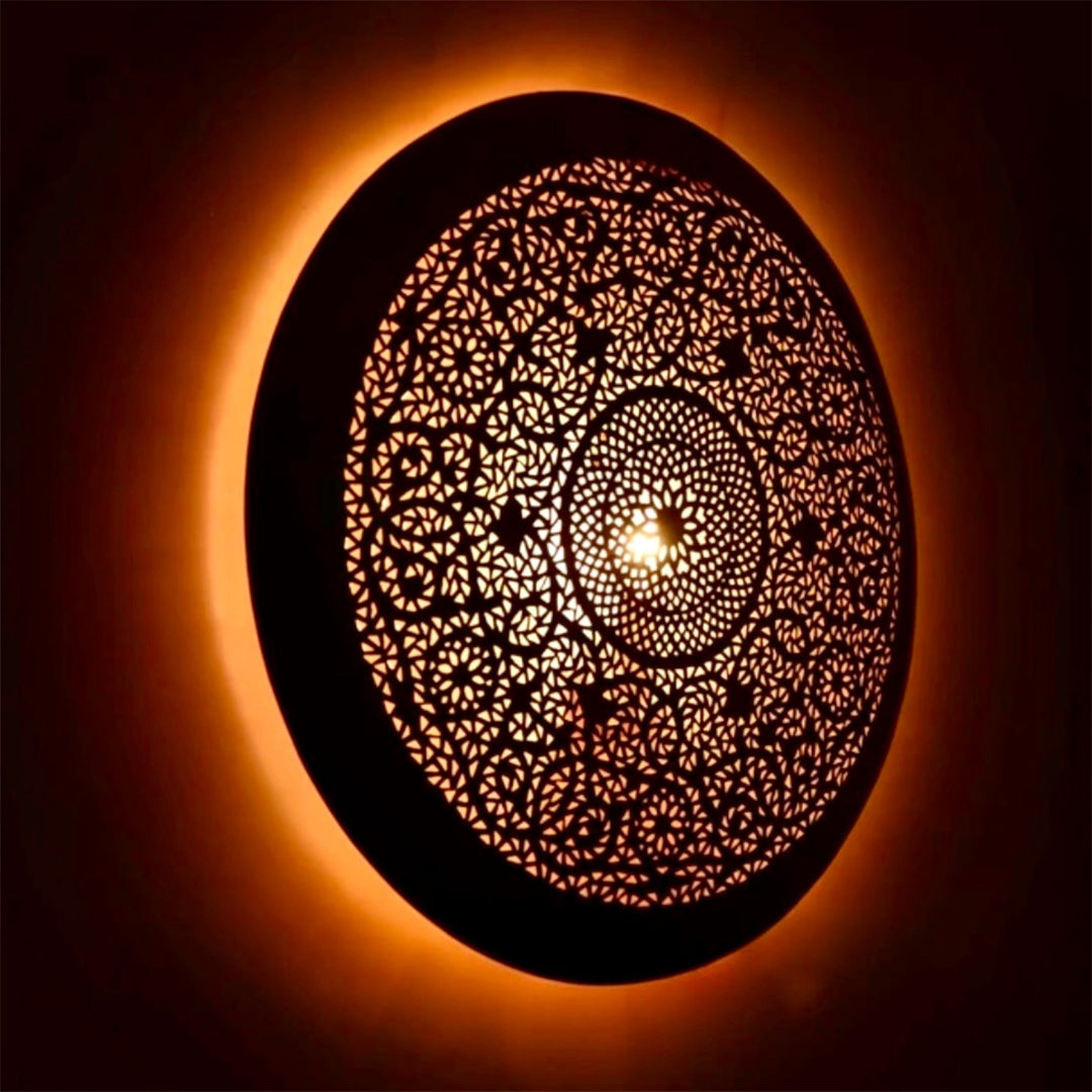 Side angle view of a modern Moroccan brass flush mount lamp illuminated, casting a soft golden glow on the wall.