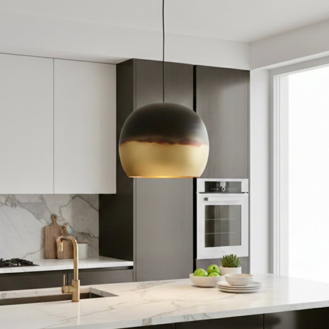 A single handmade Moroccan dome pendant light in brass and dark copper hanging over a white marble kitchen island.