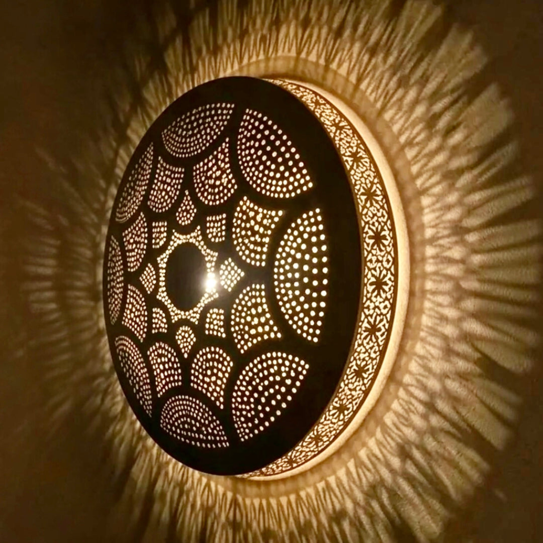Side view angle of an illuminated Moroccan brass flush mount lamp showing the detailed metal craftsmanship and radiating starburst shadow reflections.