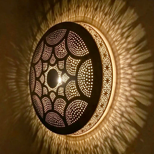 Side view angle of an illuminated Moroccan brass flush mount lamp showing the detailed metal craftsmanship and radiating starburst shadow reflections.