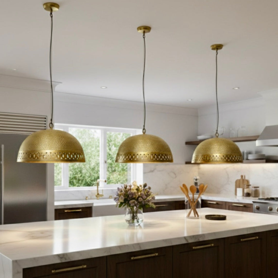 Trio of handmade hammered brass Moroccan dome pendant lights hanging over a modern marble kitchen island with dark wood cabinets.