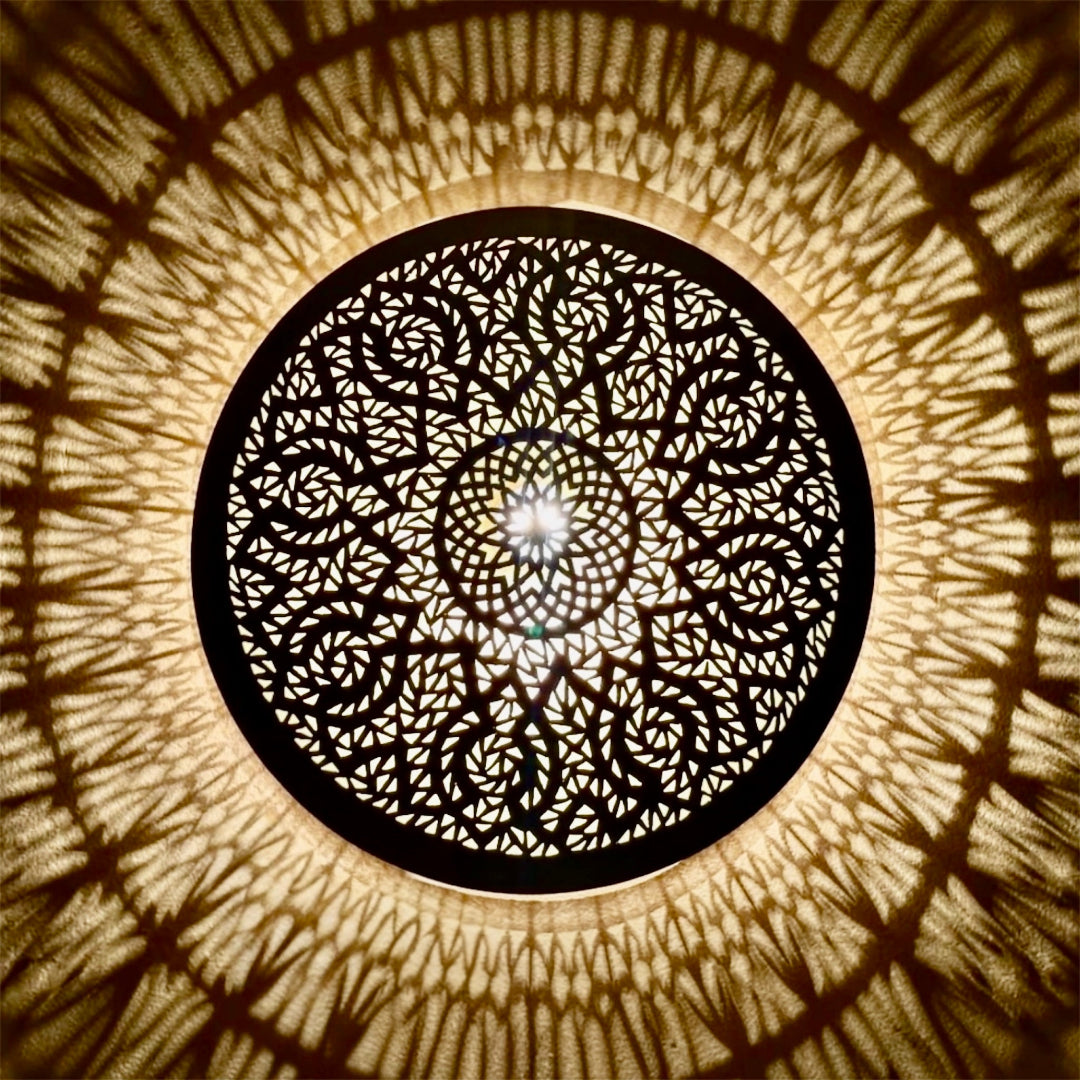  ⁠Close-up of a lit round Moroccan brass wall sconce projecting beautiful warm geometric shadow patterns on the wall.⁠