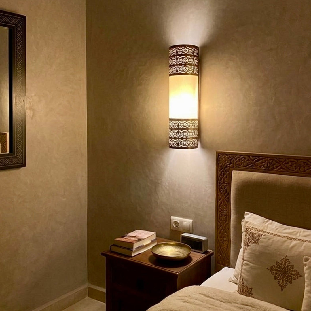  Authentic Moroccan brass wall lamp with intricate hand-carved patterns installed as a bedside reading light in a warm-toned bedroom.