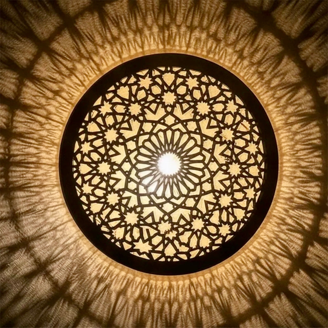 ⁠Close-up overhead view of a handcrafted Moroccan brass flush mount ceiling lamp casting an intricate geometric shadow pattern on the wall.