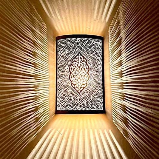 Close-up of a Moroccan brass wall lamp showing the dramatic radial shadow patterns created by the traditional hand-pierced metalwork.
