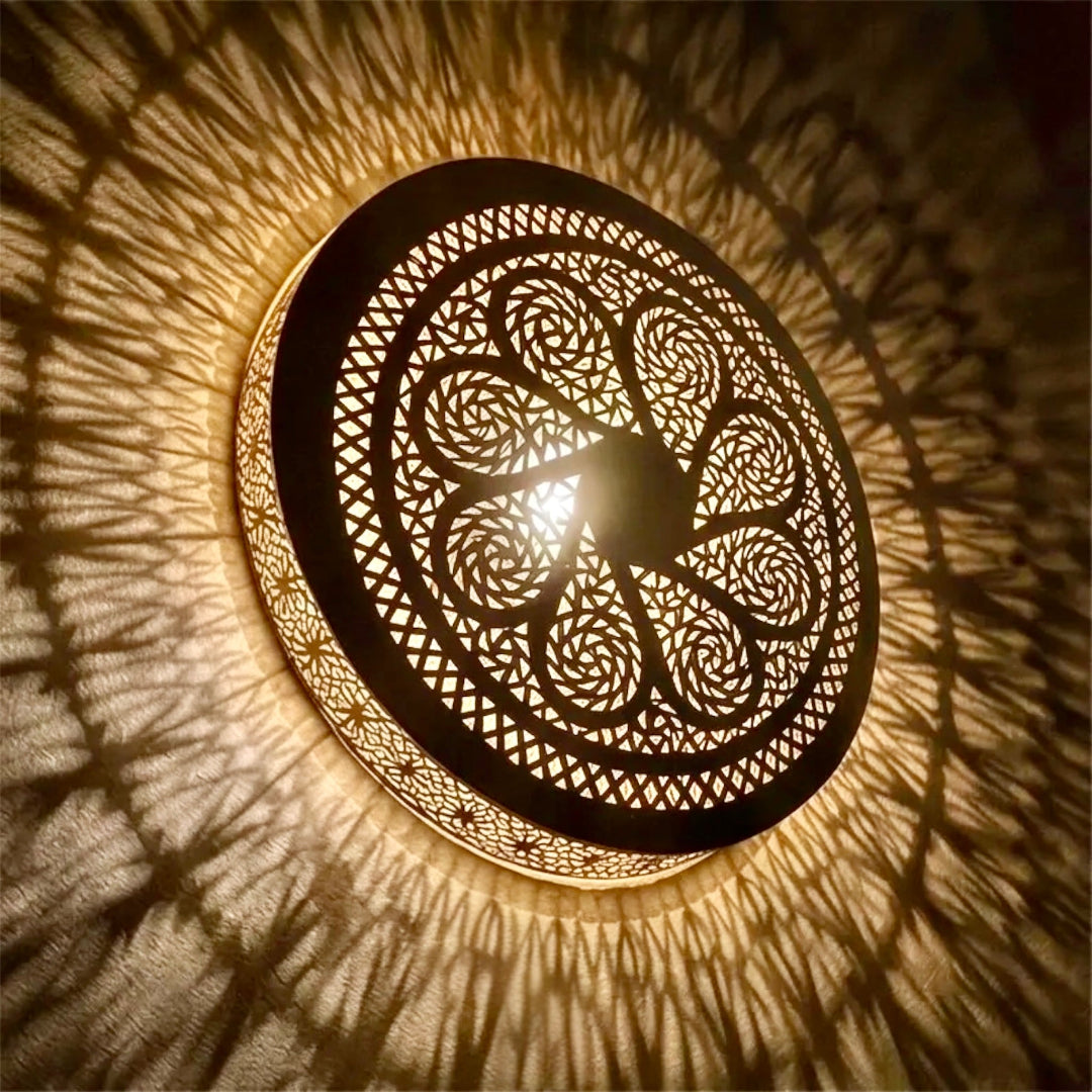 Angled view of a glowing Moroccan handmade brass flushmount lamp, highlighting the warm ambient lighting and radial shadow projection on a textured ceiling.
