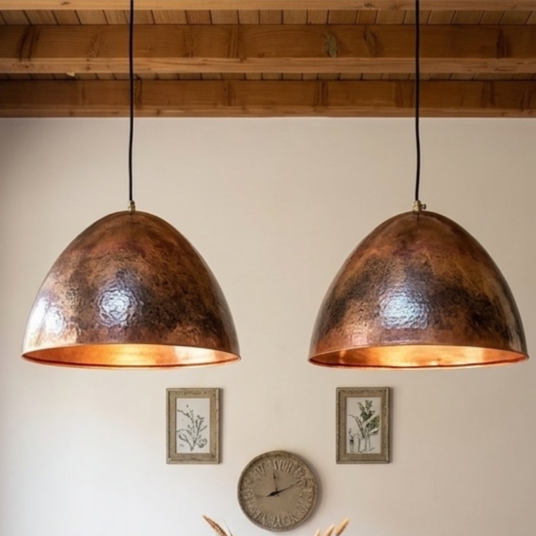 Pair of modern handmade Moroccan hammered copper dome pendant lights hanging above a wooden dining table in a minimalist dining room