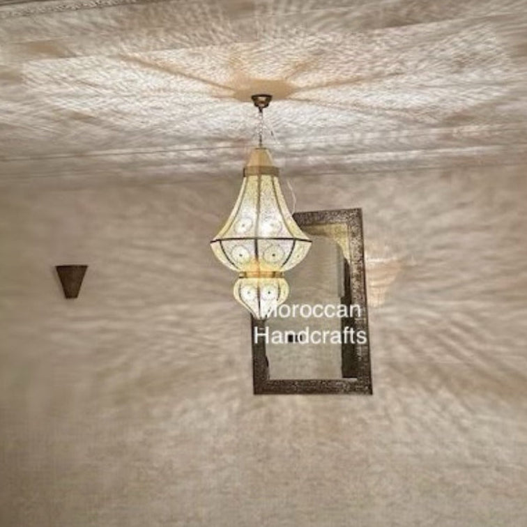  Hand-carved Moroccan pendant lamp positioned over a round wooden dining table in a contemporary restaurant setting.