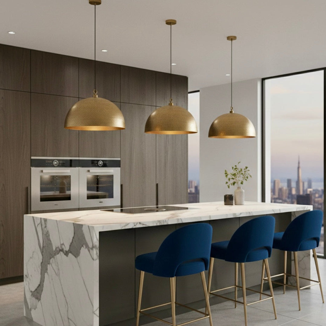 Three Moroccan-inspired brass dome pendant lamps over a large dining table with emerald green velvet chairs and patterned cream wallpaper.