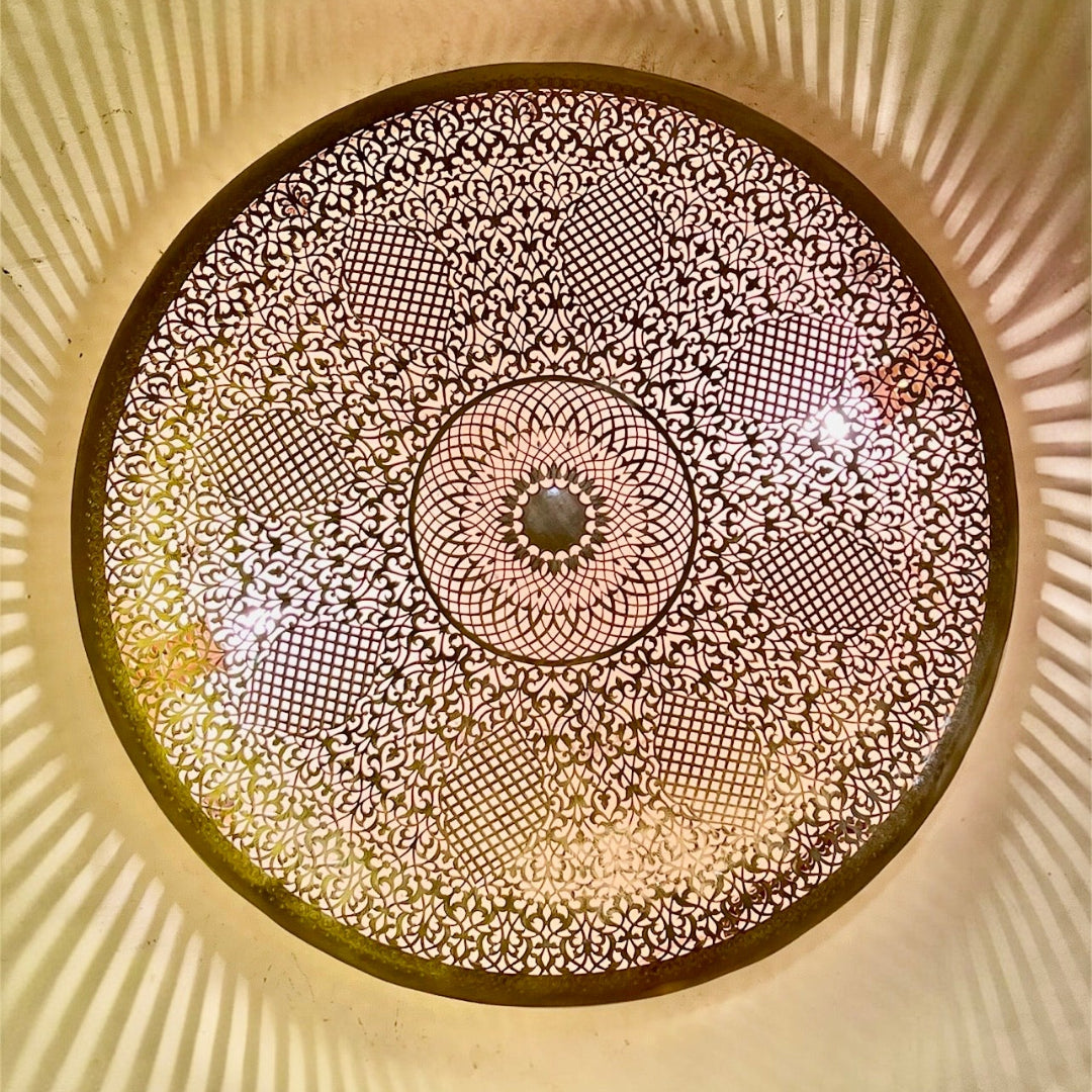 Illuminated Moroccan brass lamp casting elegant radial shadows on a wall.