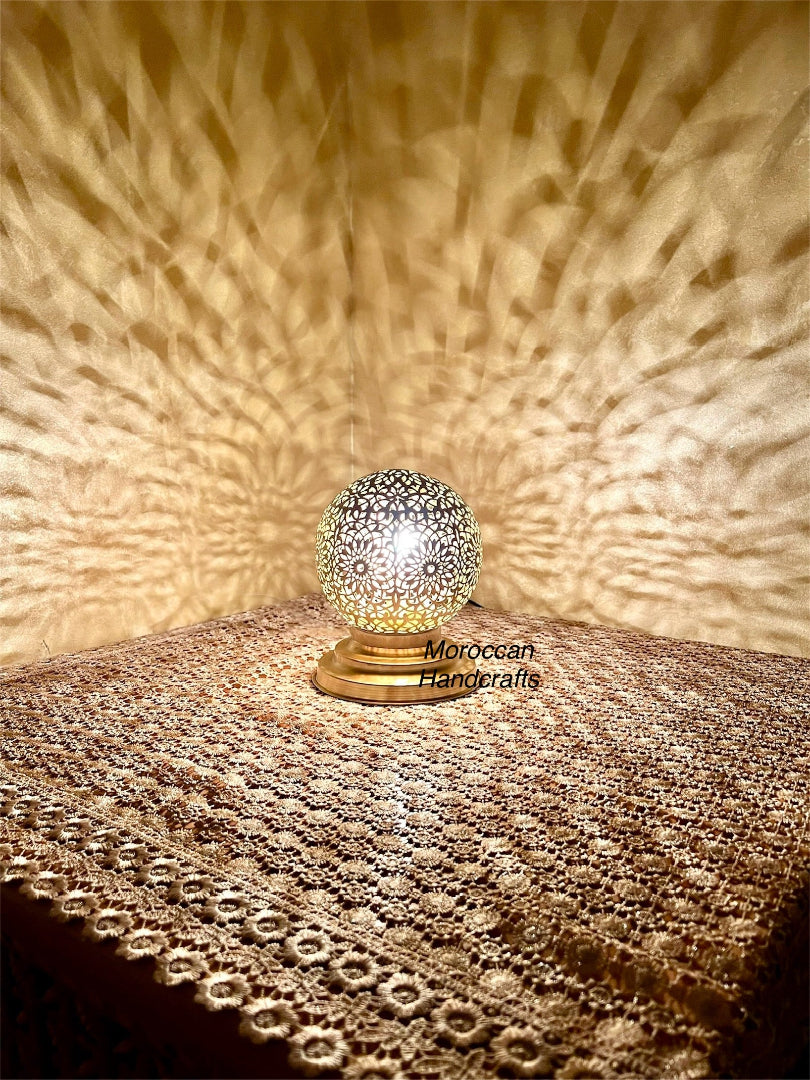 Handmade Moroccan brass table lamp casting intricate geometric shadow patterns on a gold wall.