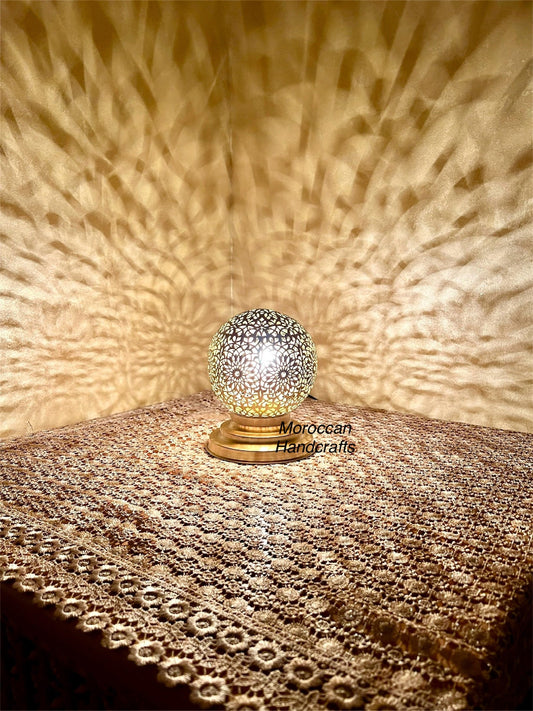 Handmade Moroccan brass table lamp casting intricate geometric shadow patterns on a gold wall.