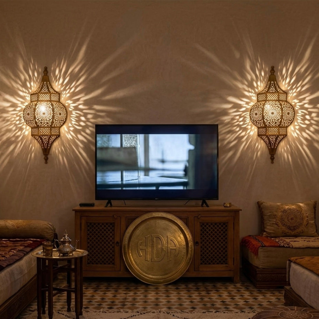 Two symmetrical handmade brass wall sconces installed on either side of a TV in a luxury home, creating a warm Bohemian atmosphere.