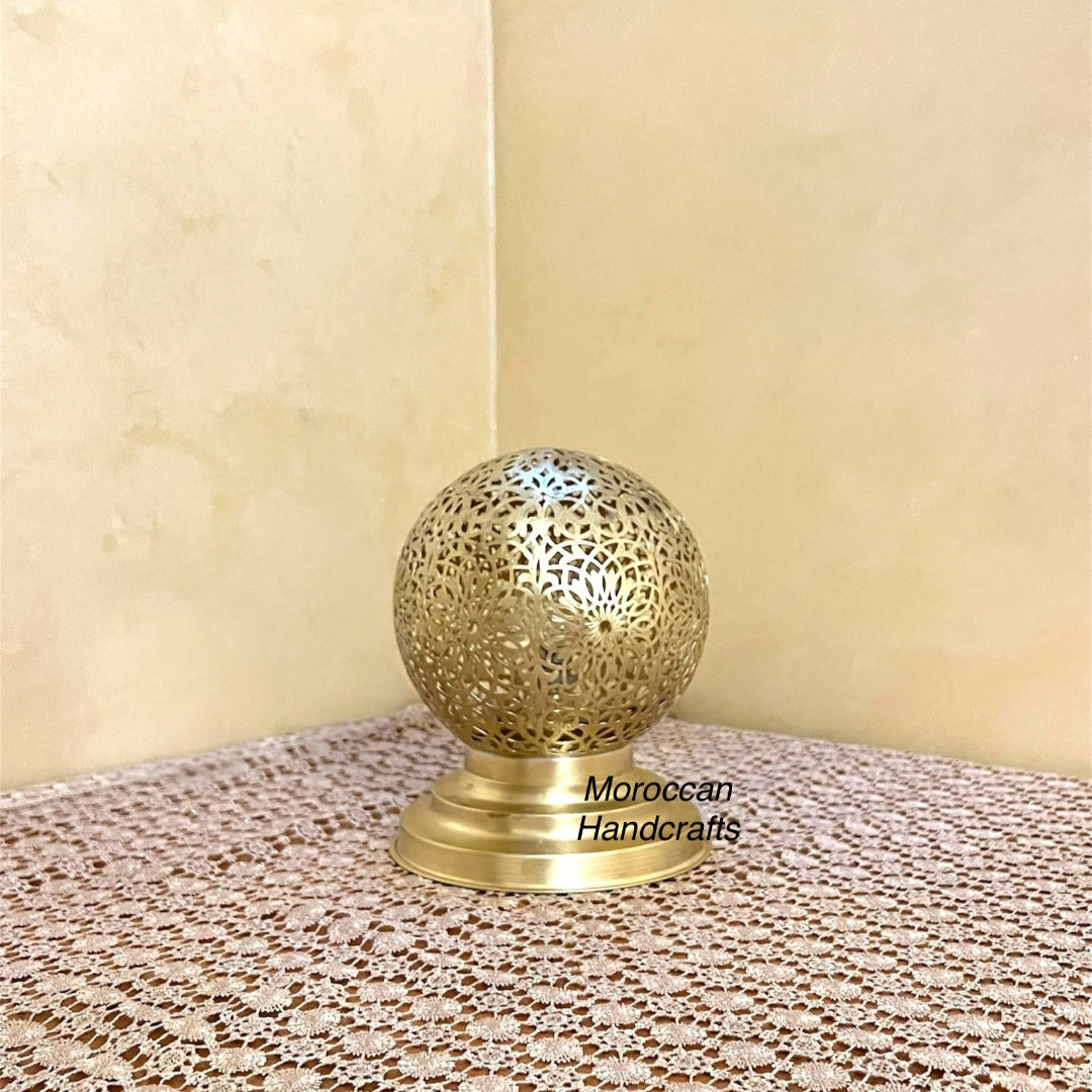Close-up of a small, traditional Moroccan perforated metal nightstand lamp with warm light.