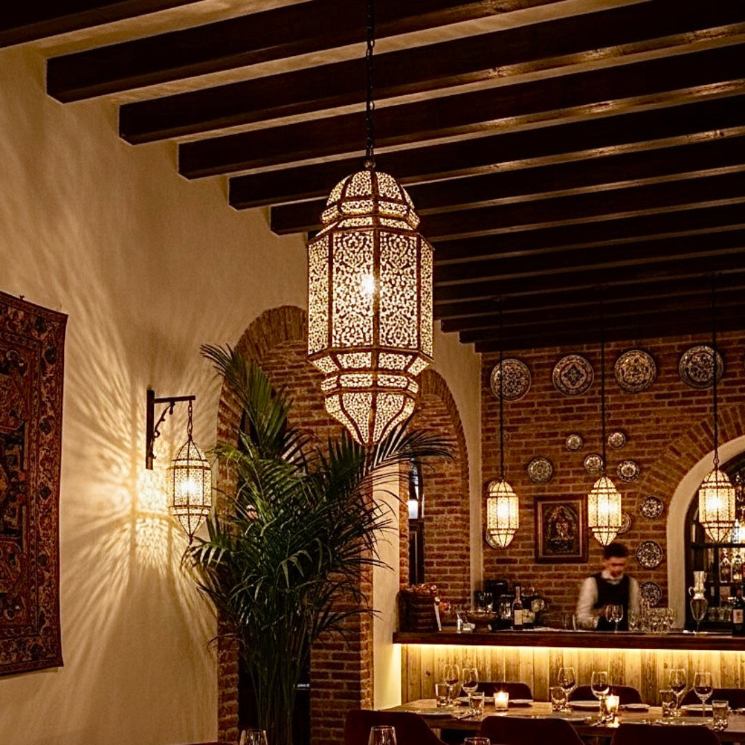 Traditional Moroccan restaurant interior with rustic brick walls, wooden ceiling beams, and stunning handcrafted brass chandeliers providing ambient lighting.