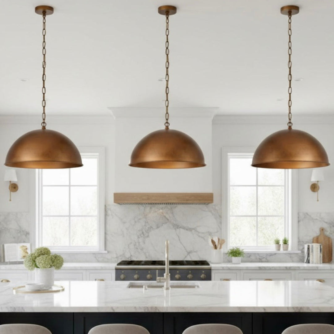 Trio of large Moroccan copper dome pendant lights installed over a white marble kitchen island.