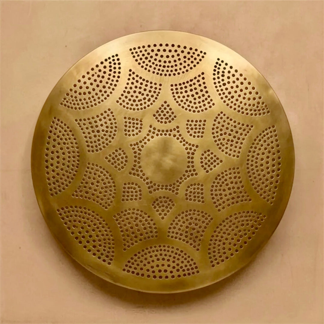  Unlit round Moroccan brass flush mount lamp fixture displaying hand-carved arabesque perforations on a minimalist plaster wall backdrop.